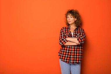 Kareli gömlek ve onun yanındaki metinle katlanmış silah için boş alan ile turuncu bir arka plan üzerinde ayakta kot çok kıvırcık kadın