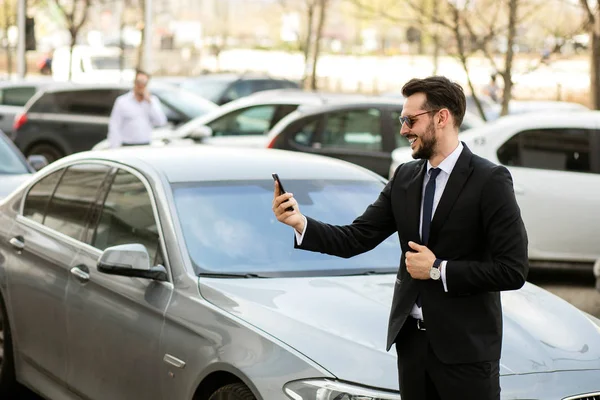 Uber sürücü bir ofis binası önünde sokakta dışında cep telefonunu, gösterilen bir lüks araba önünde şık elbiseli