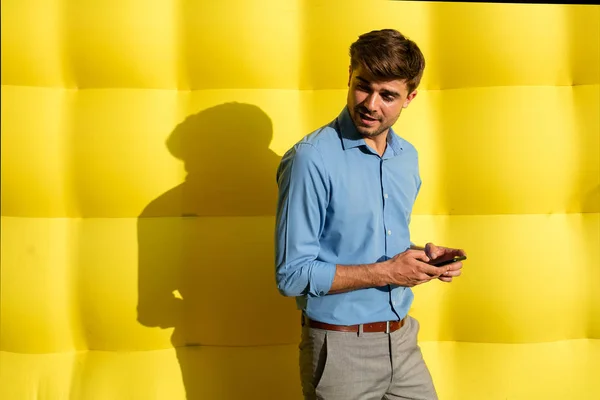 elegant smart guy with cellphone standing on a yellow background