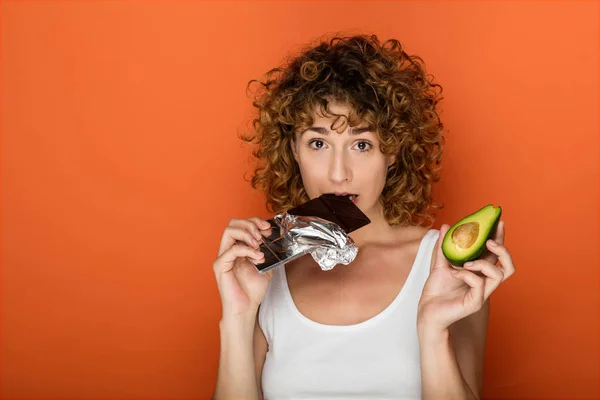 Krullend Jongedame Holding Een Avocado Chocolade Handen Een Oranje Achtergrond — Stockfoto