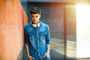 Gençler için müzik. onun boynuna bir duvara yaslanmış kulaklıklar ile kot kıyafeti içinde genç adamla kavramı