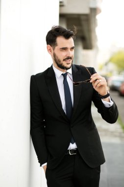 Birilerinin, beyaz bir duvar ile sunglasess karşı ayakta dışında takım, işadamı, zarif yakışıklı bekliyor