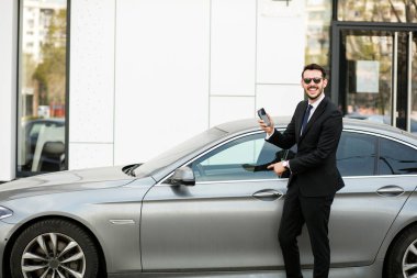 Uber sürücü bir ofis binası önünde sokakta dışında cep telefonunu, gösterilen bir lüks araba önünde şık elbiseli