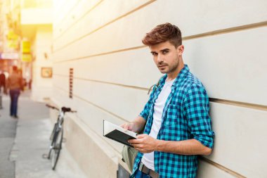 yakışıklı genç adam, öğrenci dışında bir kitap okuma bir duvara karşı duran sırt çantası ile
