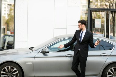 Uber sürücü bir ofis binası önünde sokakta dışında cep telefonunu, gösterilen bir lüks araba önünde şık elbiseli