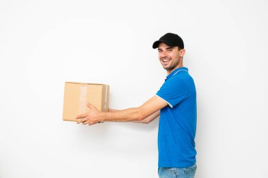 profilde ayakta ve kamera, beyaz arka plan üzerinde bakarken bir cardbox sunan teslimatçı