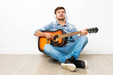 çocuklar için hobi. adam kafasına kulaklık ile gitar çalmak, yere oturmak, onun boş zamanlarında kendi evinde zevk, neden hoşlandığını, beyaz arka plan üzerinde yapıyor