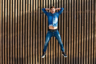 serin ve modern bir hava. ahşap arka plan üzerinde son derece mutlu neşeli tavrı ile atlama yakışıklı seksi erkek kot pantolon kıyafeti,