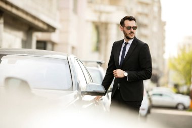 güneş gözlüğü ile takım elbise, onun lüks araba, sokakta bir şehrin içine steping emin zarif adam