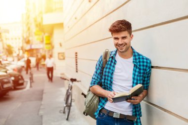 yakışıklı genç adam, öğrenci dışında bir kitap okuma bir duvara karşı duran sırt çantası ile