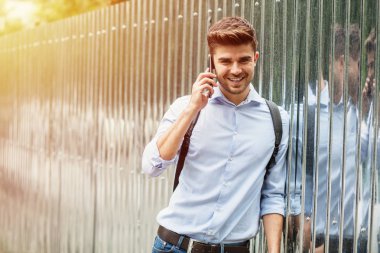 Kurumsal adam. cep telefonunu kullanarak Gri Metalik arka plan üzerinde sırt çantası ile akıllı casual adam