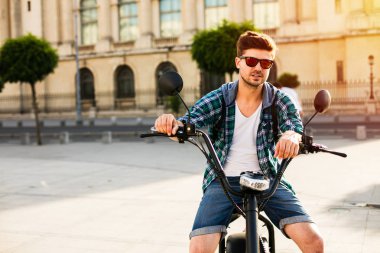 Elektrik kentsel ulaşım. seksi bir genç adam, kameraya bakarak onun elektrikli bisiklet üzerinde güneş gözlüklü cool olmak