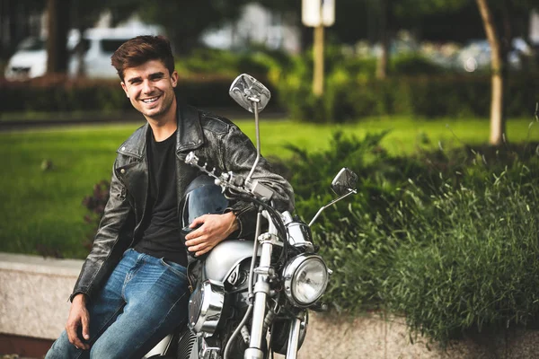 young and cool. handsome and relaxing man sitting on his motorcycle, in a city center waiting for someone