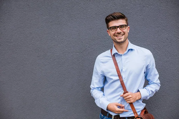 pointing the empty side. handsome smart casual man with eyeglasses and leather bag outside pointing a free space next to him with confidence and smile