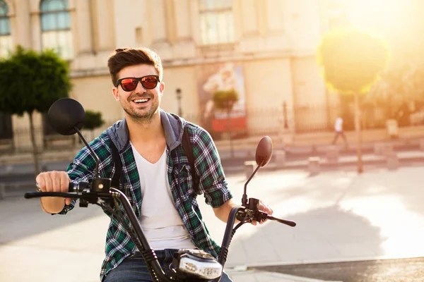 Elektrik kentsel ulaşım. Elektrikli araç, scooter, bir metropola ortasına oturan gözlüklü genç adam kameraya gülümseyen