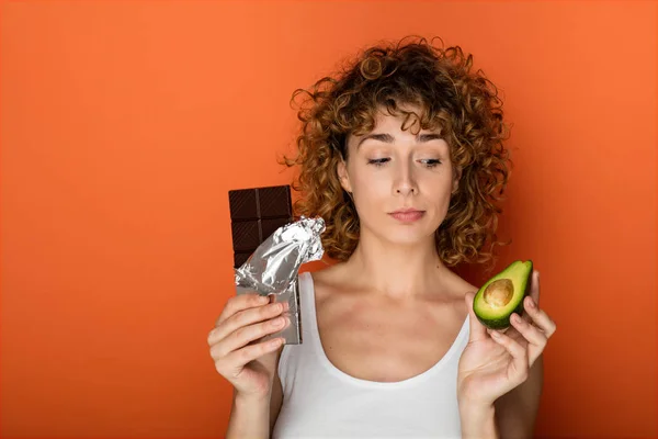 Jovem Mulher Encaracolado Segurando Abacate Chocolate Mãos Sobre Fundo Laranja — Fotografia de Stock