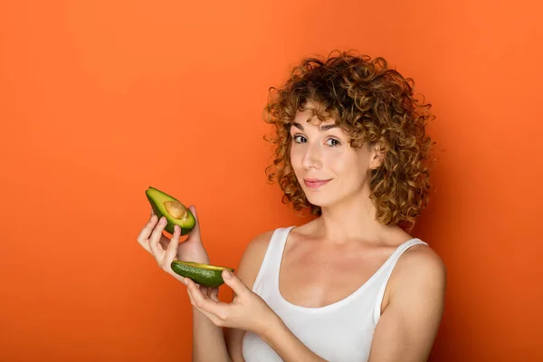 Krullend Jongedame Houden Van Een Avocado Handen Een Oranje Achtergrond — Stockfoto