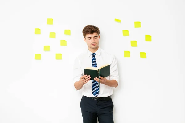 elegant man at office, lawyer or corporate guy, studing or making a research on something, holding a book in hands with many post its on wall