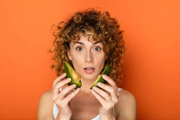 Junge Lockige Frau Mit Einer Avocado Der Hand Auf Orangefarbenem — Stockfoto