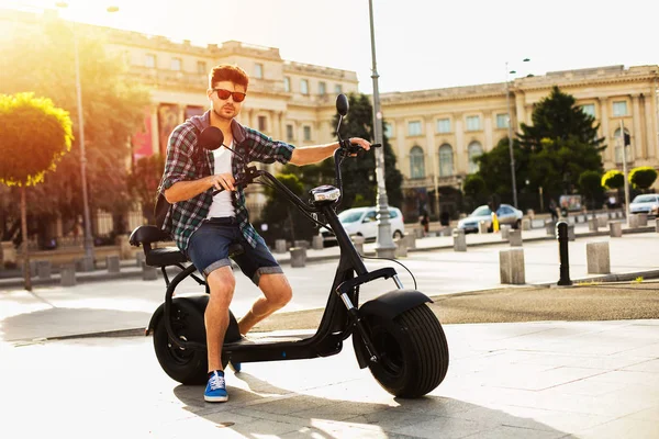 电力城市交通 英俊的年轻人 与背包和太阳镜坐在他的电动自行车 准备骑在一个晴朗的日子在市中心的城市 — 图库照片