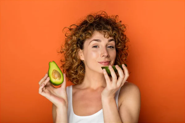 Krullend Jongedame Houden Van Een Avocado Handen Een Oranje Achtergrond — Stockfoto