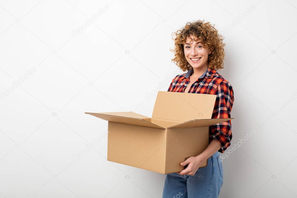 surprised young curly woman in checkered shirt standing on empty wall with some mooving boxes