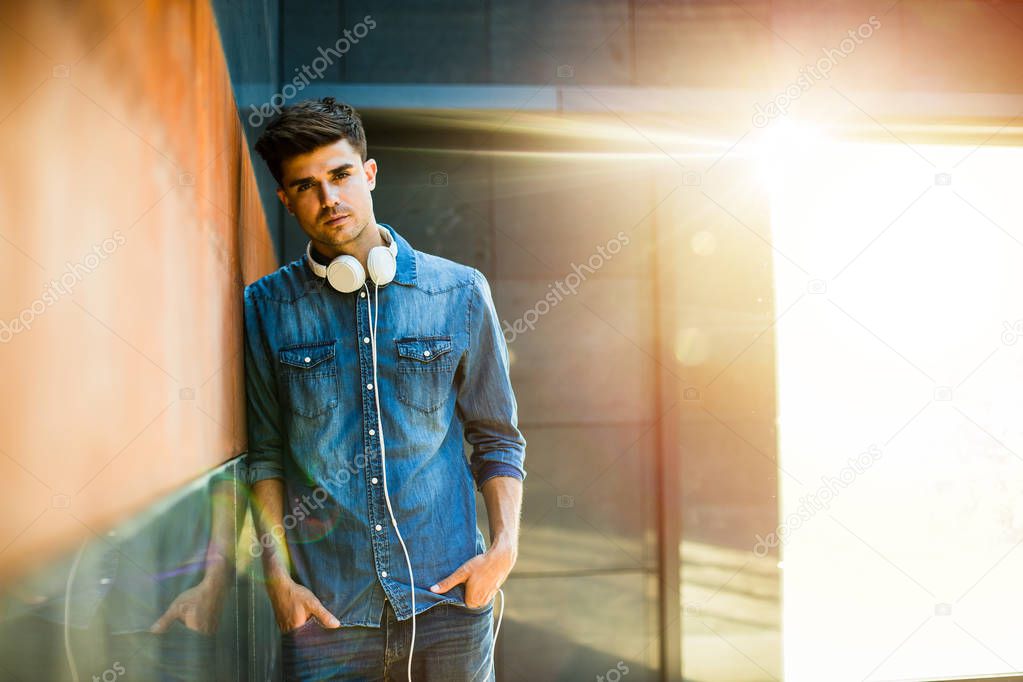 music for youngsters. concept with young guy all in jeans outfit, with headsets around his neck, leaning against a wall