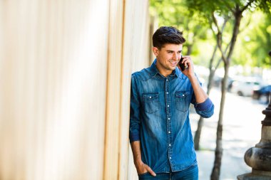 Genç adam cep telefonu konuşurken ve gülümseyen, dış mekan, ahşap çerçevede bir sokakta kot kıyafeti