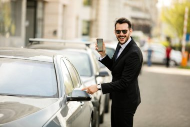 cep telefonunu gösterilen ve fotoğraf gülümseyen güzel elbiseli şık adam arabasını dor açıyor