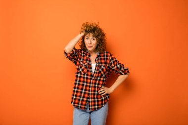 Kareli gömlek ve onun yanındaki metin için boş alan ile turuncu bir arka plan üzerinde ayakta kot heyecanlı kıvırcık kadın