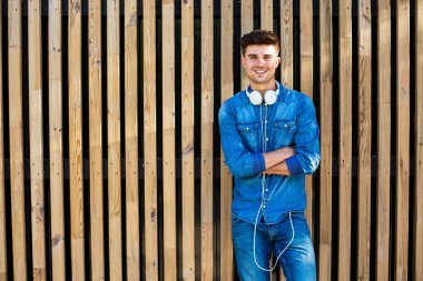 serin ve modern. yakışıklı seksi adam onu kendine güvenen ve neşeli ve boynunda kulaklıklarla ayakta yanındaki metni için boş alan ile ahşap arka plan üzerinde kot kıyafeti