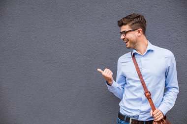 Boş tarafı işaret. yakışıklı zeki casual adam gözlük ve güven ve gülümseme ile boş bir alan onun yanında işaret dışında deri çanta