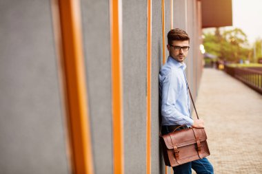 zor bir gün. yakışıklı zeki casual adam gözlük ve güven ile kamera için dışarıda bir gri duvara oturan mavi gömlek ile