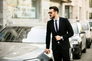 güneş gözlüğü ile takım elbise, onun lüks araba, sokakta bir şehrin içine steping emin zarif adam