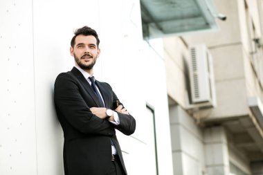 ayakta dışında takım, işadamı, zarif yakışıklı birini, sunglasess ile beyaz bir duvara katlanmış silah ile kameraya gülümseyen bekledi