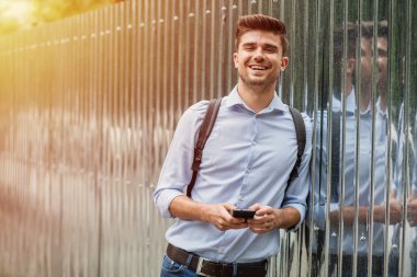 Kurumsal adam. cep telefonunu kullanarak Gri Metalik arka plan üzerinde sırt çantası ile akıllı casual adam