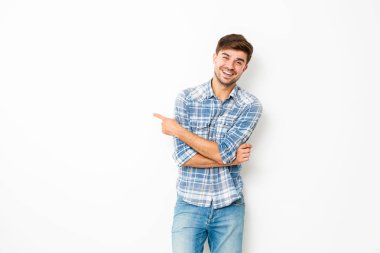 tatlı çocuk, kot pantolon ve kareli gömlek boş uzayda ile beyaz duvarda duran, bir tarafı işaret eden genç adam