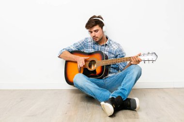 çocuklar için hobi. adam kafasına kulaklık ile gitar çalmak, yere oturmak, onun boş zamanlarında kendi evinde zevk, neden hoşlandığını, beyaz arka plan üzerinde yapıyor