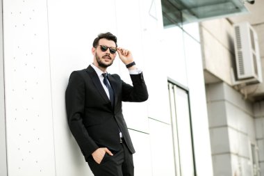 zarif yakışıklı güneş gözlüklerini ayakta dışında bir iş parkta bir duvara, ayarlama