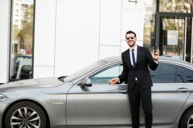 Uber sürücü bir ofis binası önünde sokakta dışında cep telefonunu, gösterilen bir lüks araba önünde şık elbiseli