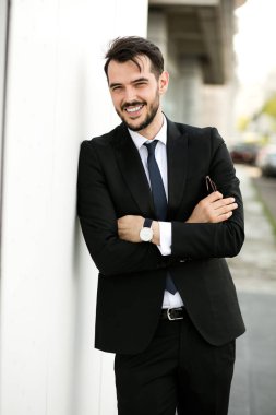 ayakta dışında takım, işadamı, zarif yakışıklı birini, sunglasess ile beyaz bir duvara katlanmış silah ile kameraya gülümseyen bekledi