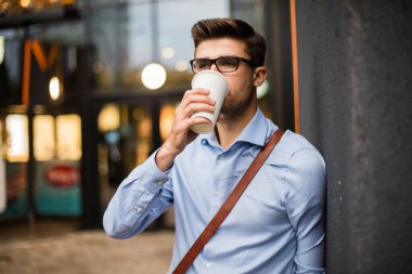 Caffee ara. yakışıklı zeki casual adam gözlük ve deri çanta dışında kentsel alanda take away kahve içer