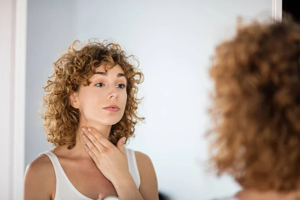 young curly woman using skin cream on in a mirror