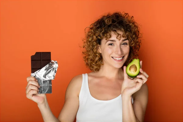 Jovem Mulher Encaracolado Segurando Abacate Chocolate Mãos Sobre Fundo Laranja — Fotografia de Stock