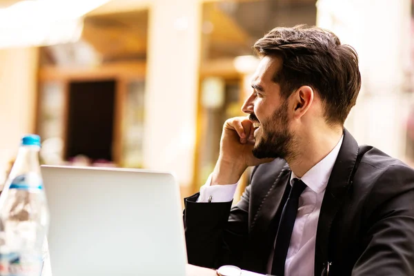 Portrait of handsome successful man with laptop in front, business man having a good conversation at mobile phone and looking to side at terrace in some old town