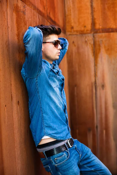 ジーンズの服装とさびた壁に立っているサングラスの若いセクシーな男 — ストック写真