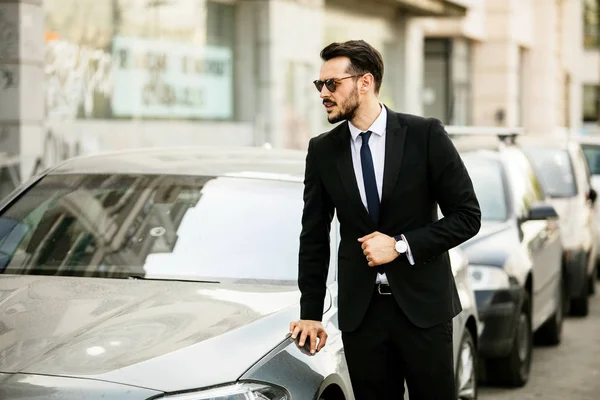 güneş gözlüğü ile takım elbise, onun lüks araba, sokakta bir şehrin içine steping emin zarif adam