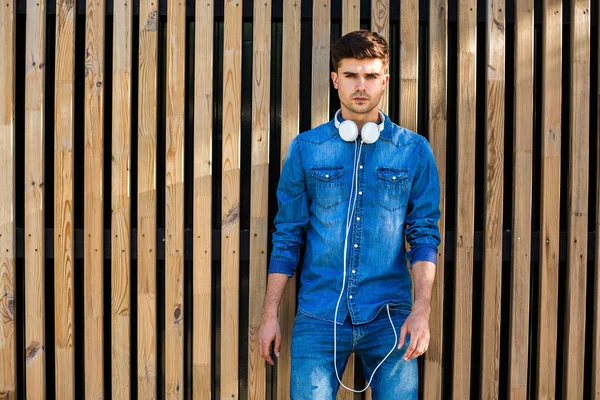 クールでモダンです 自信を持って 彼の首にヘッドフォンで陽気に立って 彼の横にテキストに空きの木製の背景にジーンズの格好をしているハンサムなセクシーな男 — ストック写真