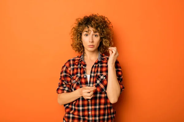 格子縞のシャツとジーンズの彼女の隣の文字列に 空のスペースでオレンジ色の背景の上に立ってかなり巻き毛の女性 — ストック写真