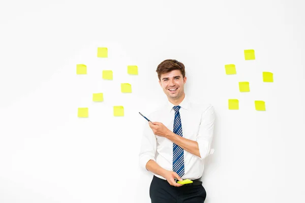 office guy at work, pointing a post it on white wall, reminder notes, plans and  objectives